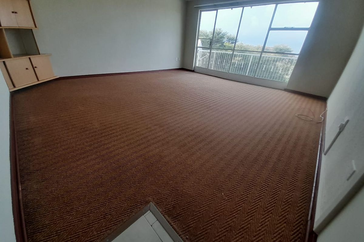Spacious living area featuring large sliding glass doors leading to a balcony, with neutral walls and carpeted flooring throughout.