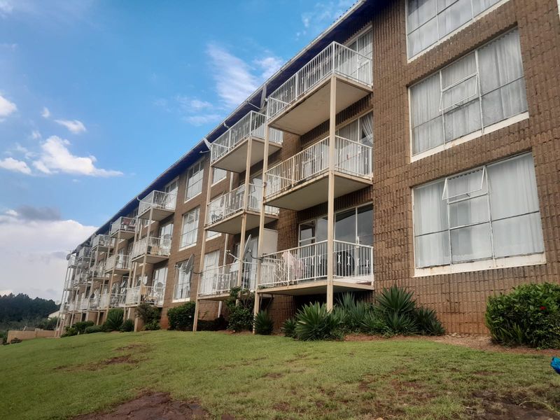 Exterior view of a multi-story apartment building featuring a brick facade, private balconies with metal railings, and large sliding glass doors.