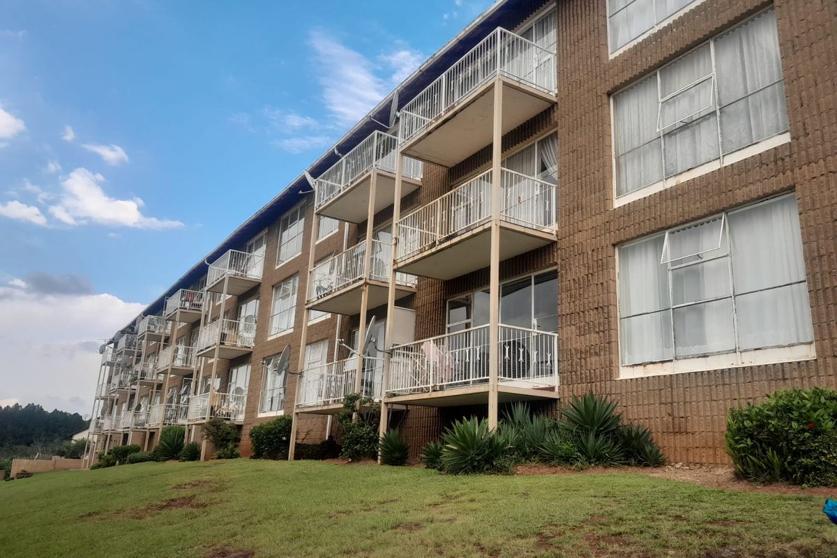 Exterior view of a multi-story apartment building featuring a brick facade, private balconies with metal railings, and large sliding glass doors.