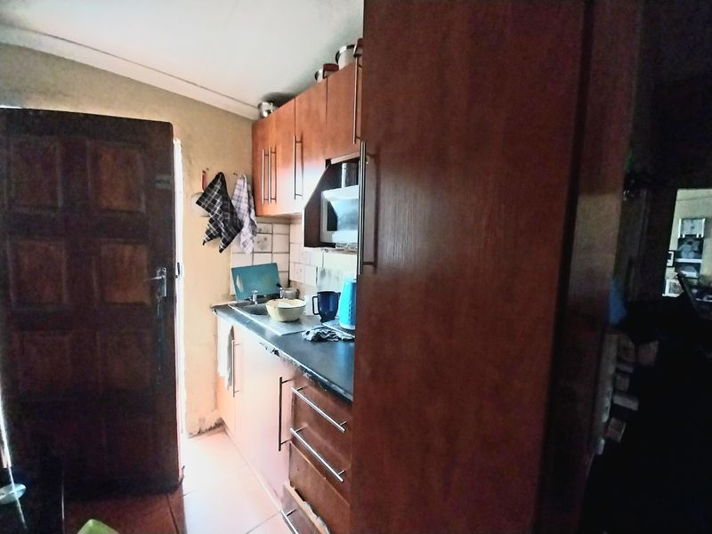 A compact kitchen featuring wooden cabinetry, a built-in sink, and tiled splashbacks, providing a functional workspace with direct access to an exterior door.