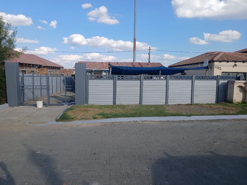 Front view of the property featuring a grey perimeter fence, metal gate, and paved driveway area.