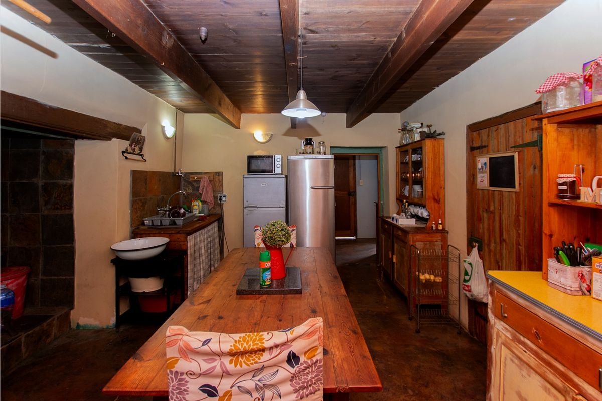 Rustic kitchen featuring exposed timber ceiling beams, stone tile backsplash, and a functional layout with integrated sink and cabinetry.