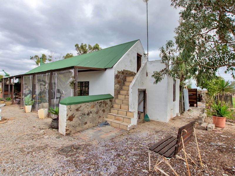 Rear view of a rustic small holding cottage featuring a green corrugated metal roof, external staircase, and a covered patio area with weather screens.