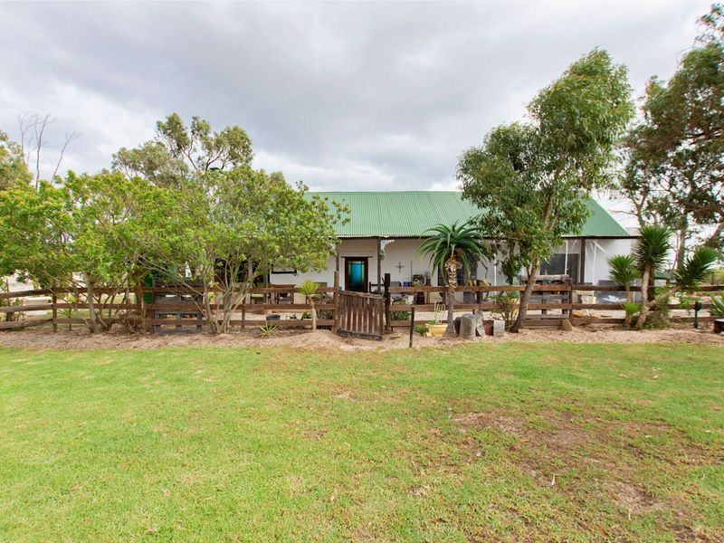 A charming small holding farmhouse featuring a green corrugated metal roof, a covered veranda, and a rustic timber fence enclosing the front garden area.