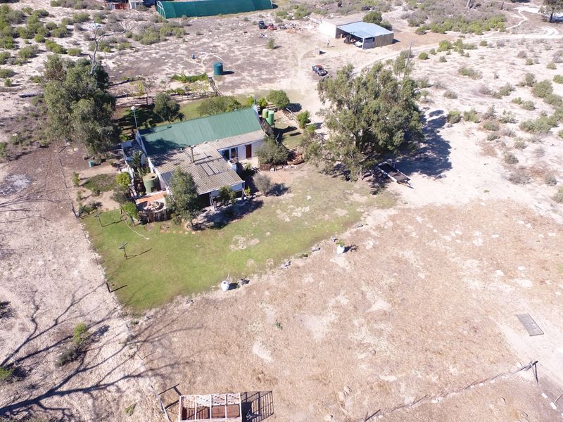 Aerial view of a small holding property featuring a main dwelling with a metal roof, surrounding garden area, water tanks, and various outbuildings.