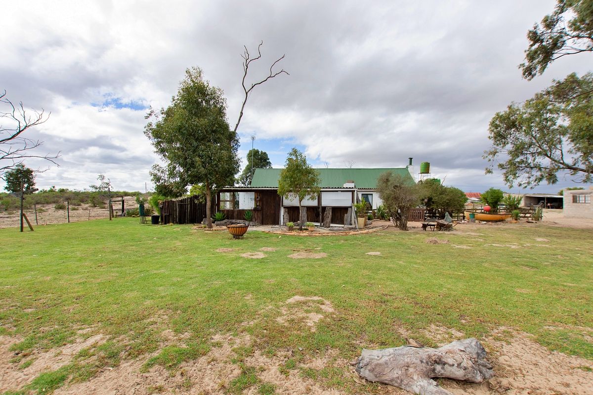 Rear view of a small holding property featuring a corrugated metal roof, timber exterior cladding, and an expansive garden area with a water tank.