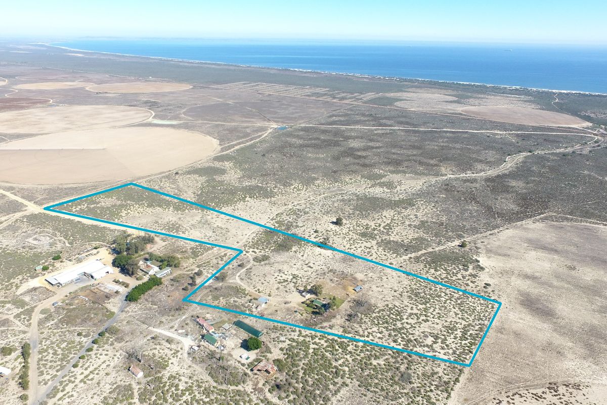 An aerial view of a large coastal small holding property, showcasing the expansive land, surrounding landscape, and existing outbuildings.