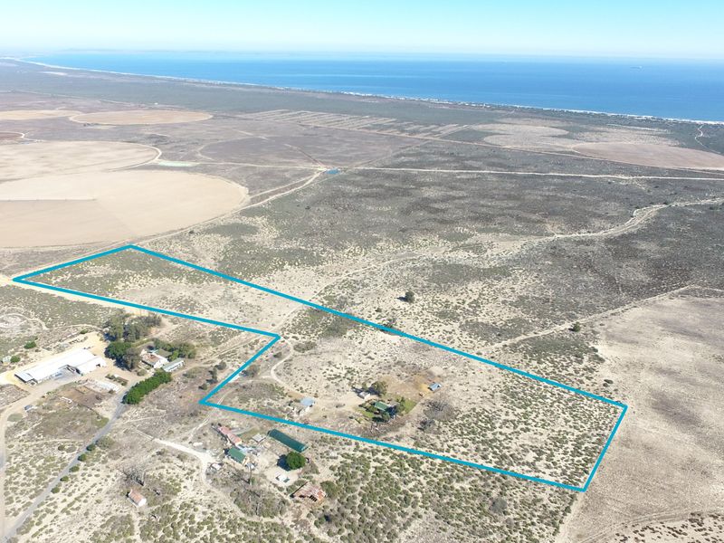 An aerial view of a large coastal small holding property, showcasing the expansive land, surrounding landscape, and existing outbuildings.