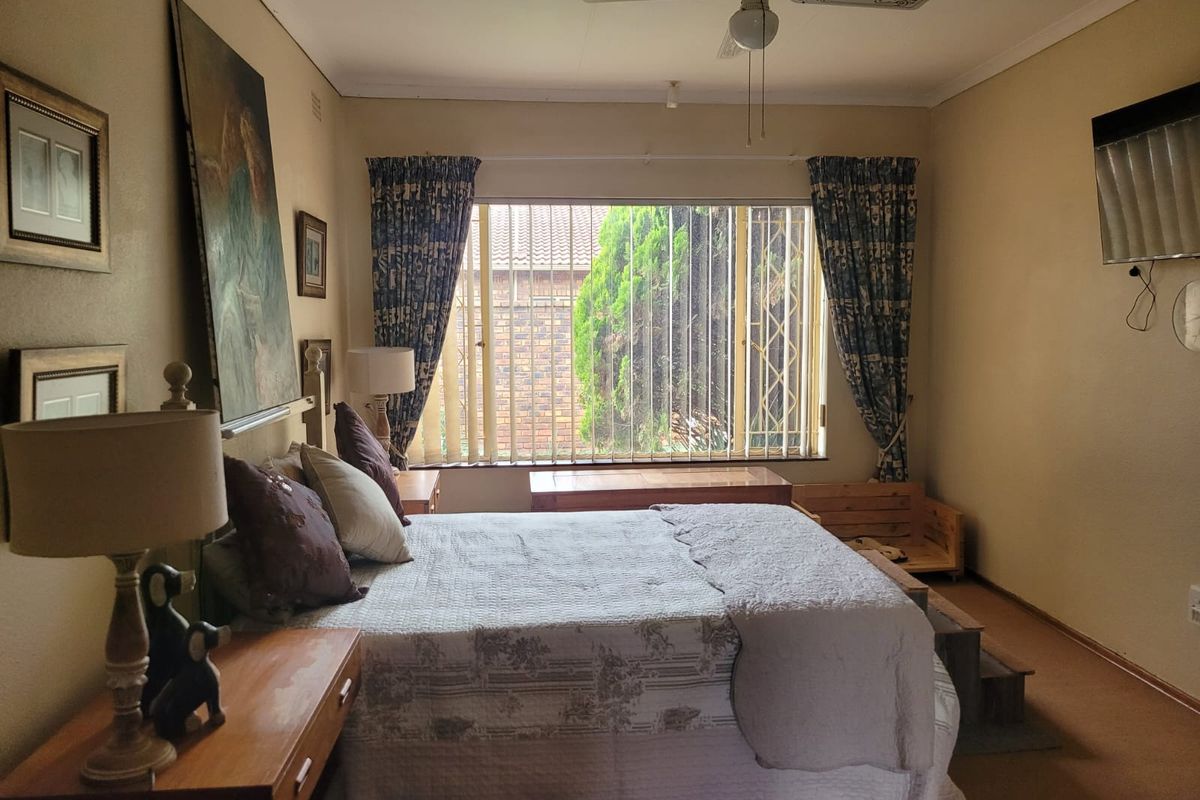 A standard bedroom featuring carpeted flooring, a ceiling fan, and large windows fitted with security bars.