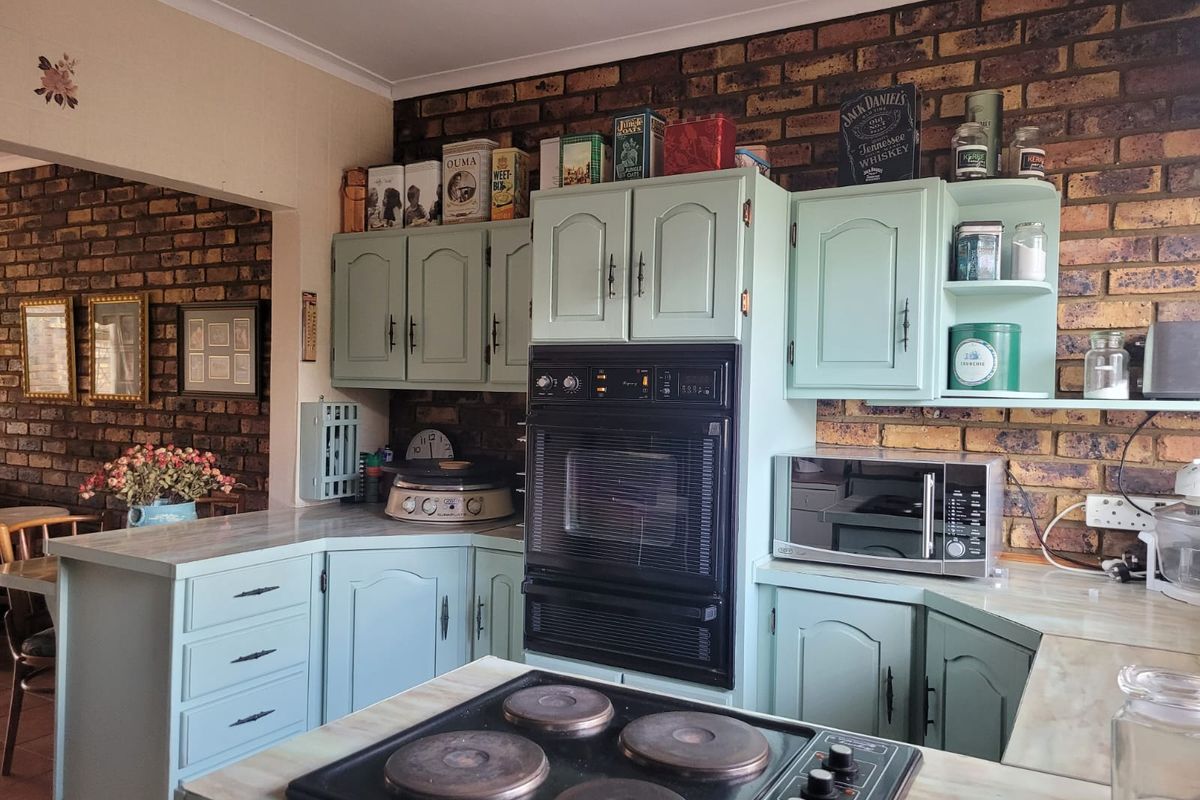 Kitchen featuring light green cabinetry, exposed brick walls, built-in oven, and electric hob with laminate countertops.