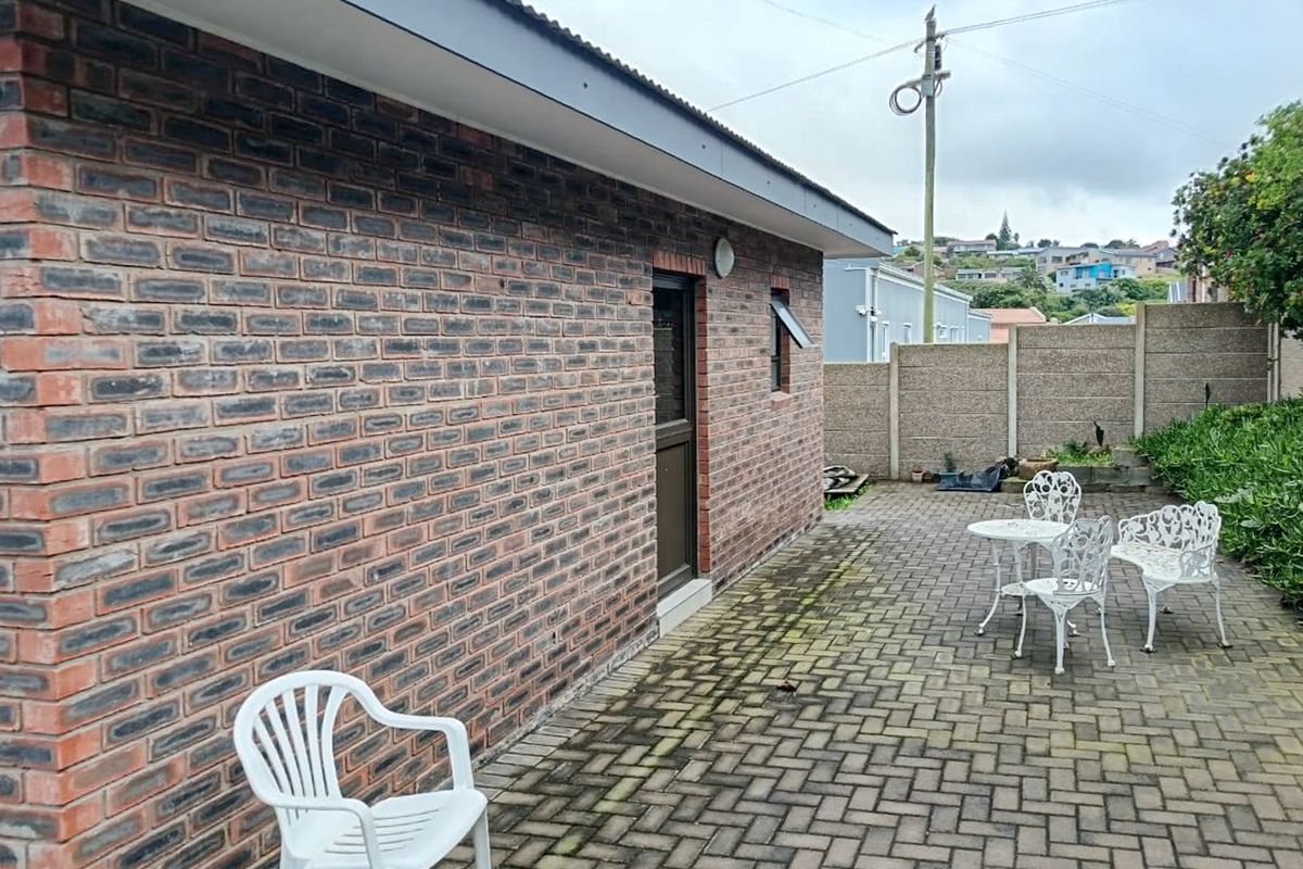 A rear exterior view featuring a face brick wall, corrugated roof, and a paved patio area enclosed by a precast concrete boundary wall.