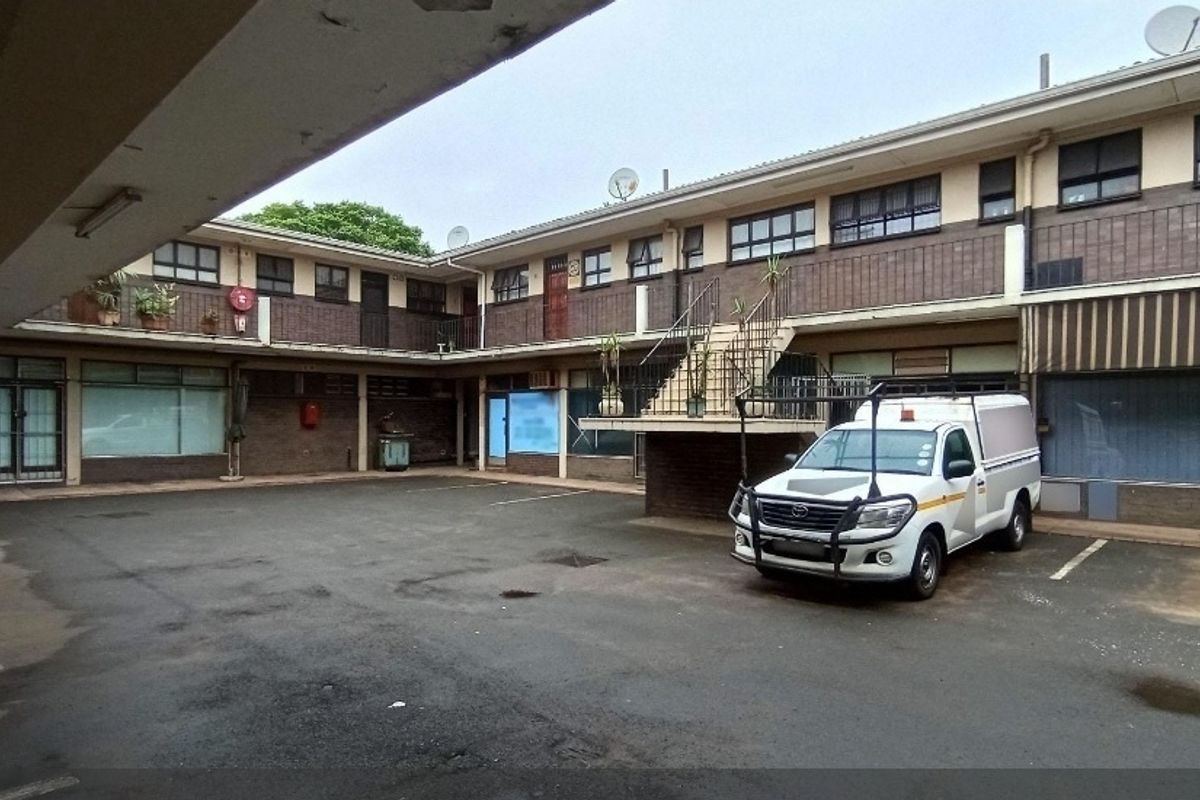 An exterior view of an apartment complex courtyard featuring an asphalt parking area, brick facade, and a central concrete staircase.
