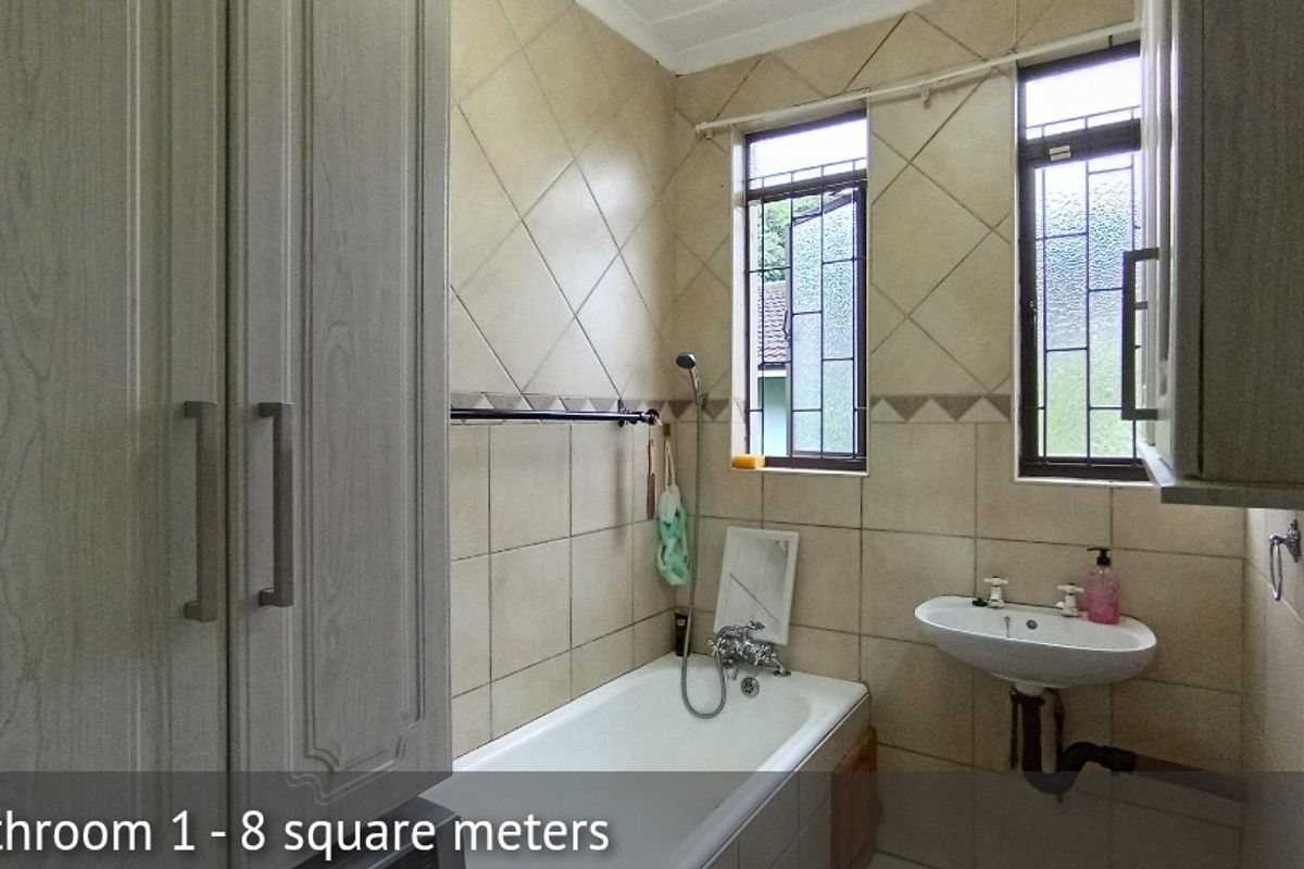 A functional bathroom featuring tiled walls, a built-in bathtub with shower mixer, a wall-mounted basin, and ample built-in storage cabinetry.