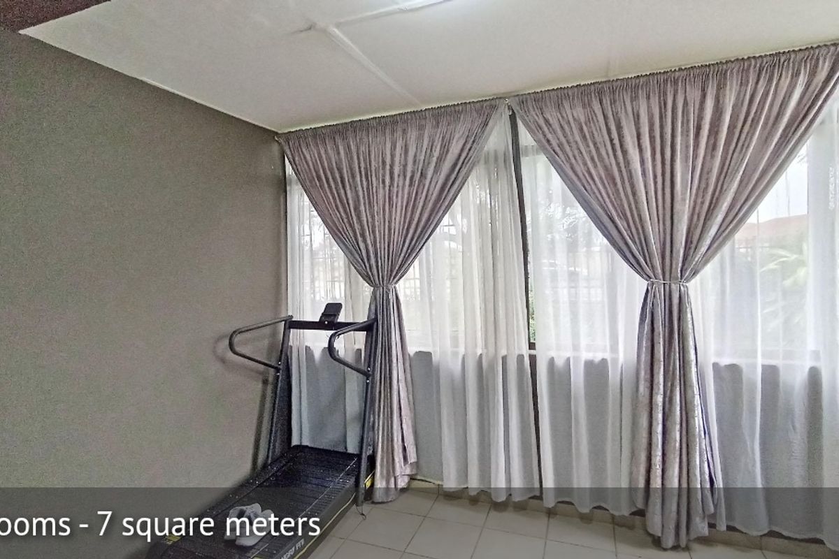 A compact bedroom or study area featuring tiled flooring and large windows with security bars, providing natural light.