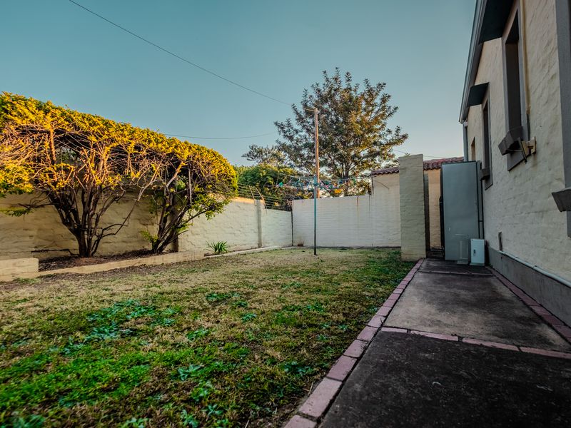 A private rear garden area featuring a lawn, concrete pathway, perimeter wall with electric fencing, and a fixed rotary washing line.