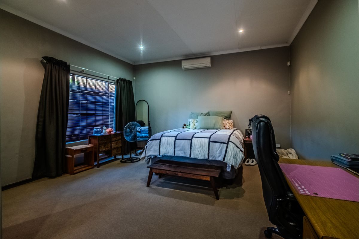 A spacious bedroom featuring neutral wall tones, carpeted flooring, recessed lighting, and a wall-mounted air conditioning unit.
