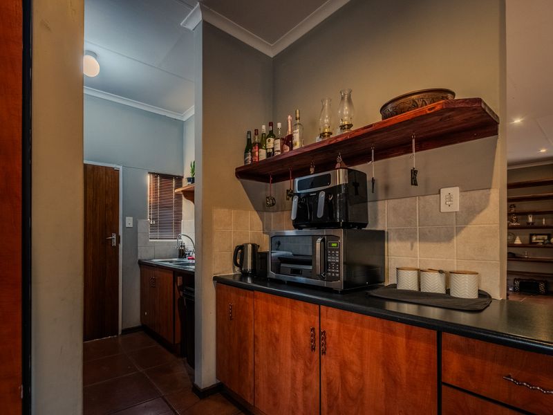 A functional scullery area featuring wood-finish cabinetry, dark laminate countertops, a tiled backsplash, and a stainless steel sink with a view to the exterior.