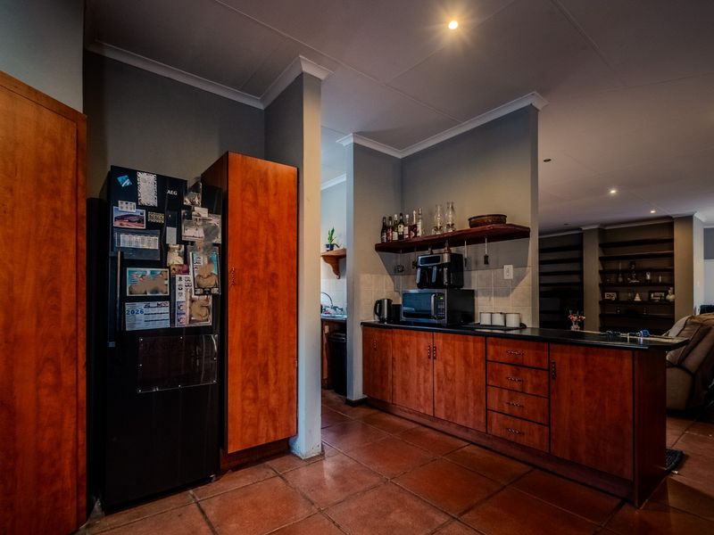 A functional kitchen featuring warm-toned wooden cabinetry, dark countertops, and tiled flooring, with an open-plan layout connecting to the living area.