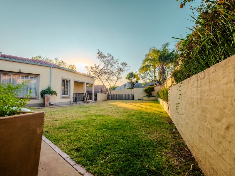A well-maintained rear garden featuring a lawn, boundary wall, and a covered patio area attached to the main dwelling.