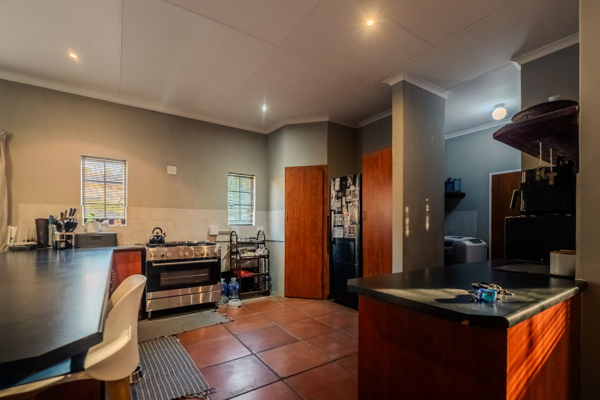 A functional kitchen featuring tiled flooring, built-in wooden cabinetry, dark countertops, and a gas stove, with an adjacent scullery area visible.