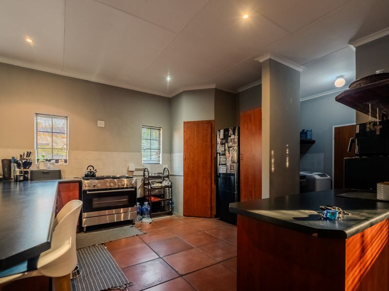 A functional kitchen featuring tiled flooring, built-in wooden cabinetry, dark countertops, and a gas stove, with an adjacent scullery area visible.