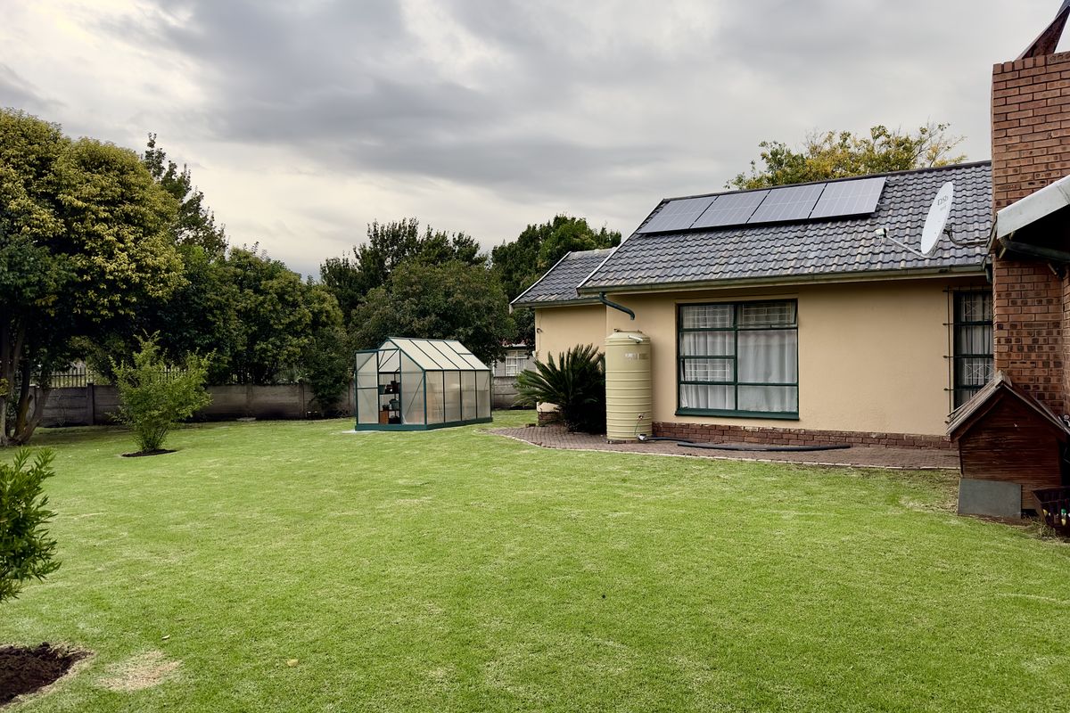 A spacious rear garden featuring a well-maintained lawn, a greenhouse, a water storage tank, and roof-mounted solar panels on the house exterior.