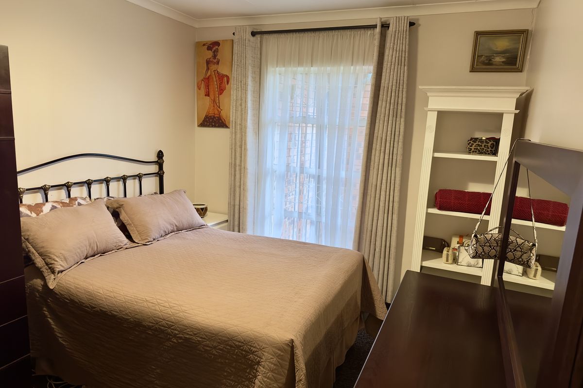 A cozy bedroom featuring neutral wall tones, carpeted flooring, and a window with curtain treatments, providing a comfortable and functional sleeping space.
