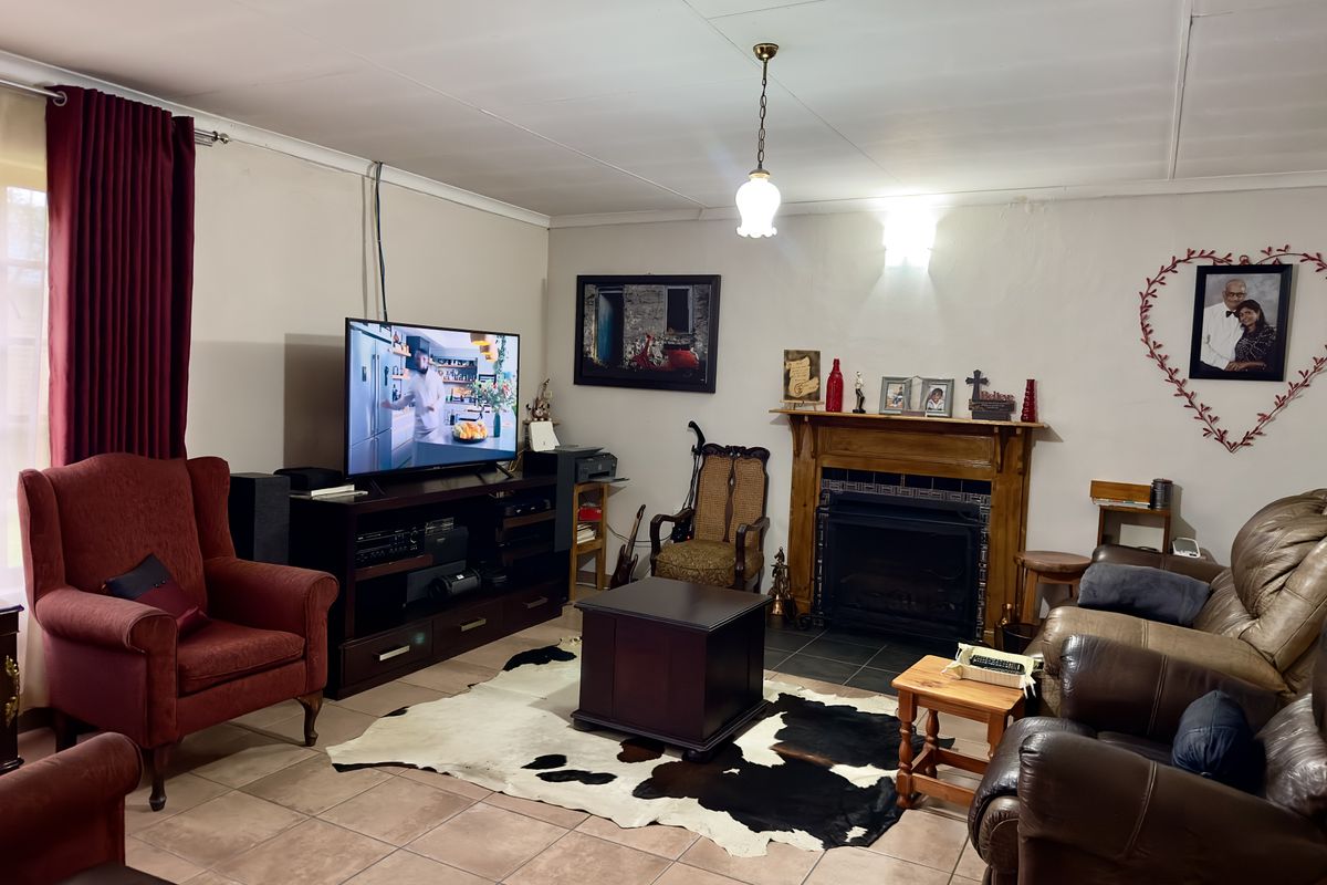 A comfortable living room featuring a traditional fireplace with a wooden mantle, tiled flooring, and a central pendant light fixture.