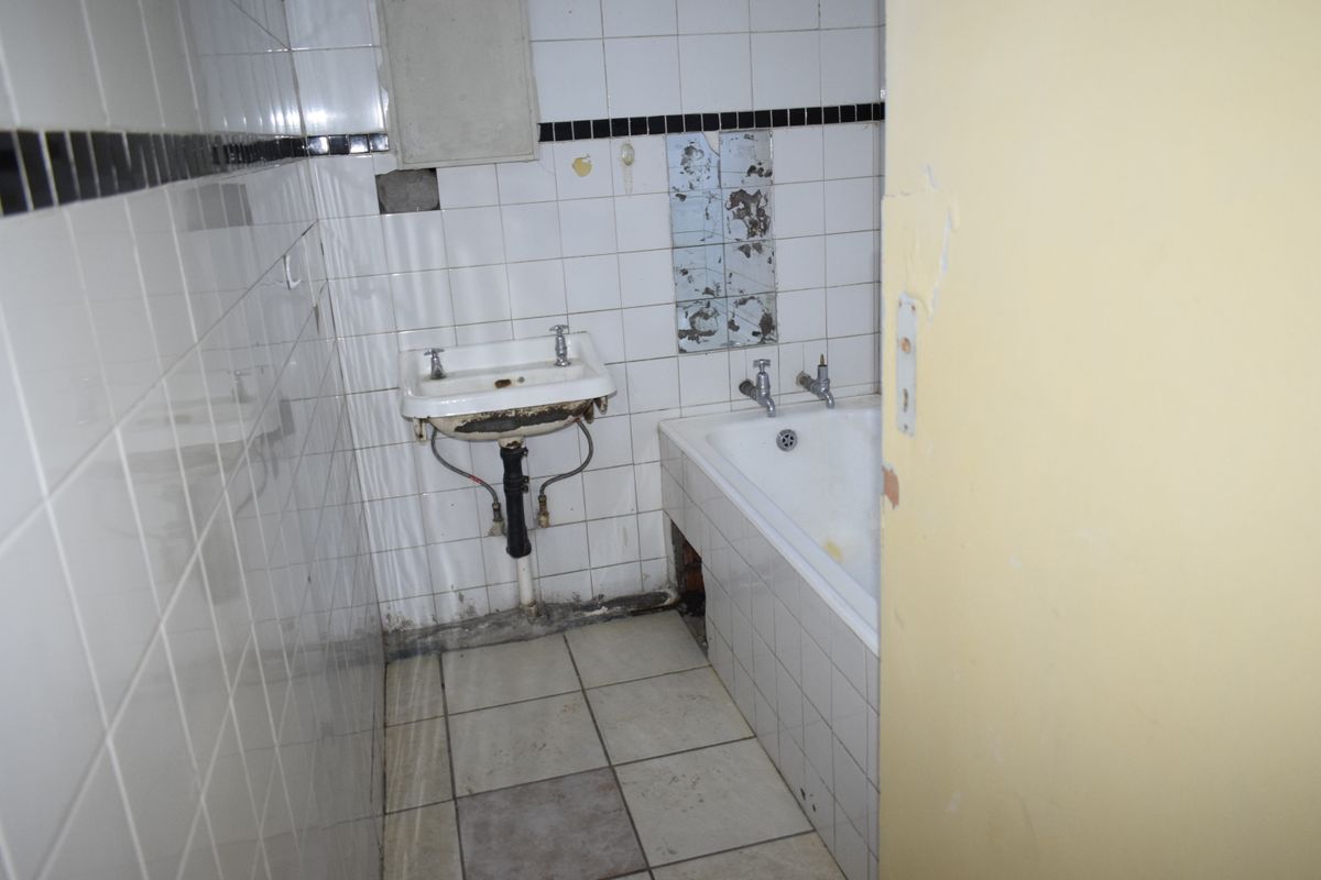 A dated bathroom featuring a wall-mounted basin and built-in bathtub, requiring significant renovation and repair to the tiling and fixtures.