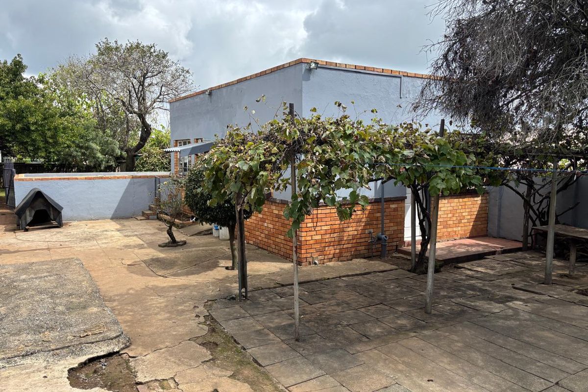 Rear exterior view of the property featuring a paved courtyard area, brick wall construction, and a vine-covered pergola structure.