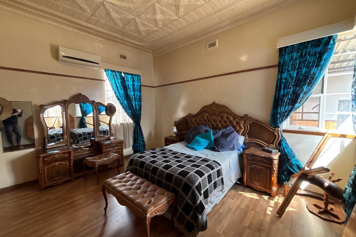 A spacious bedroom featuring a decorative pressed metal ceiling, timber-look flooring, and a wall-mounted air conditioning unit.