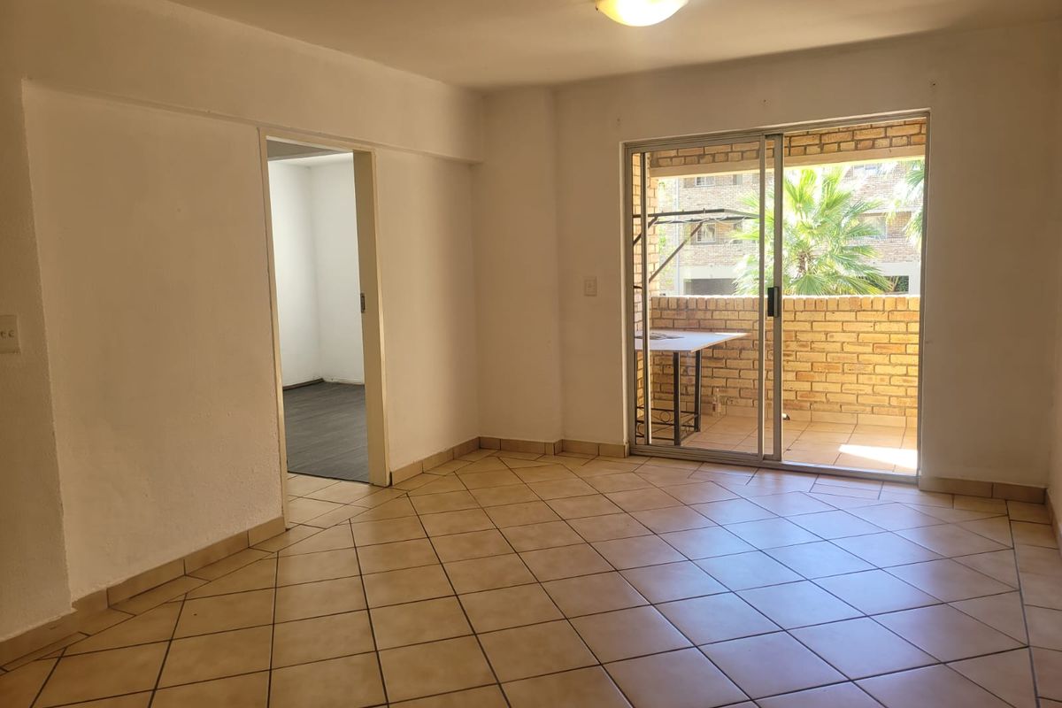 A bright, open-plan living area featuring ceramic floor tiles and sliding glass doors that open onto a private balcony.