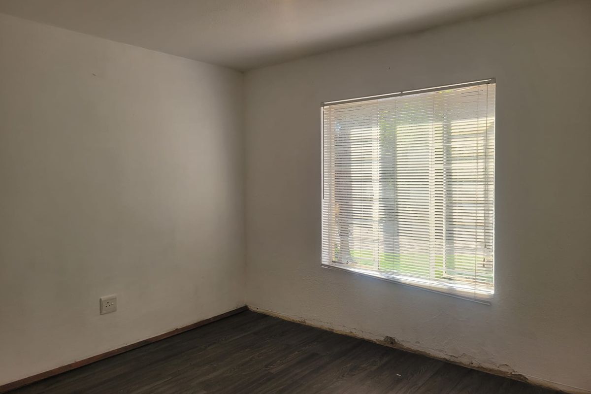 An empty bedroom featuring dark wood-look flooring, white walls, and a window fitted with horizontal blinds.