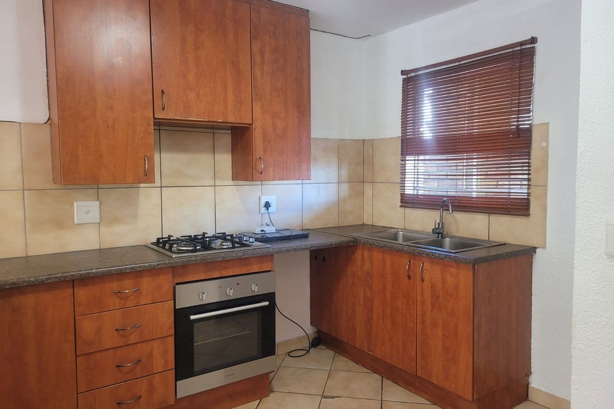 A functional kitchen featuring wooden cabinetry, a built-in oven, gas hob, double sink, and tiled splashbacks.