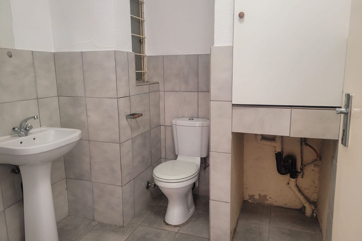 A functional bathroom featuring a pedestal basin, toilet, and an open vanity area with exposed plumbing requiring cosmetic attention.
