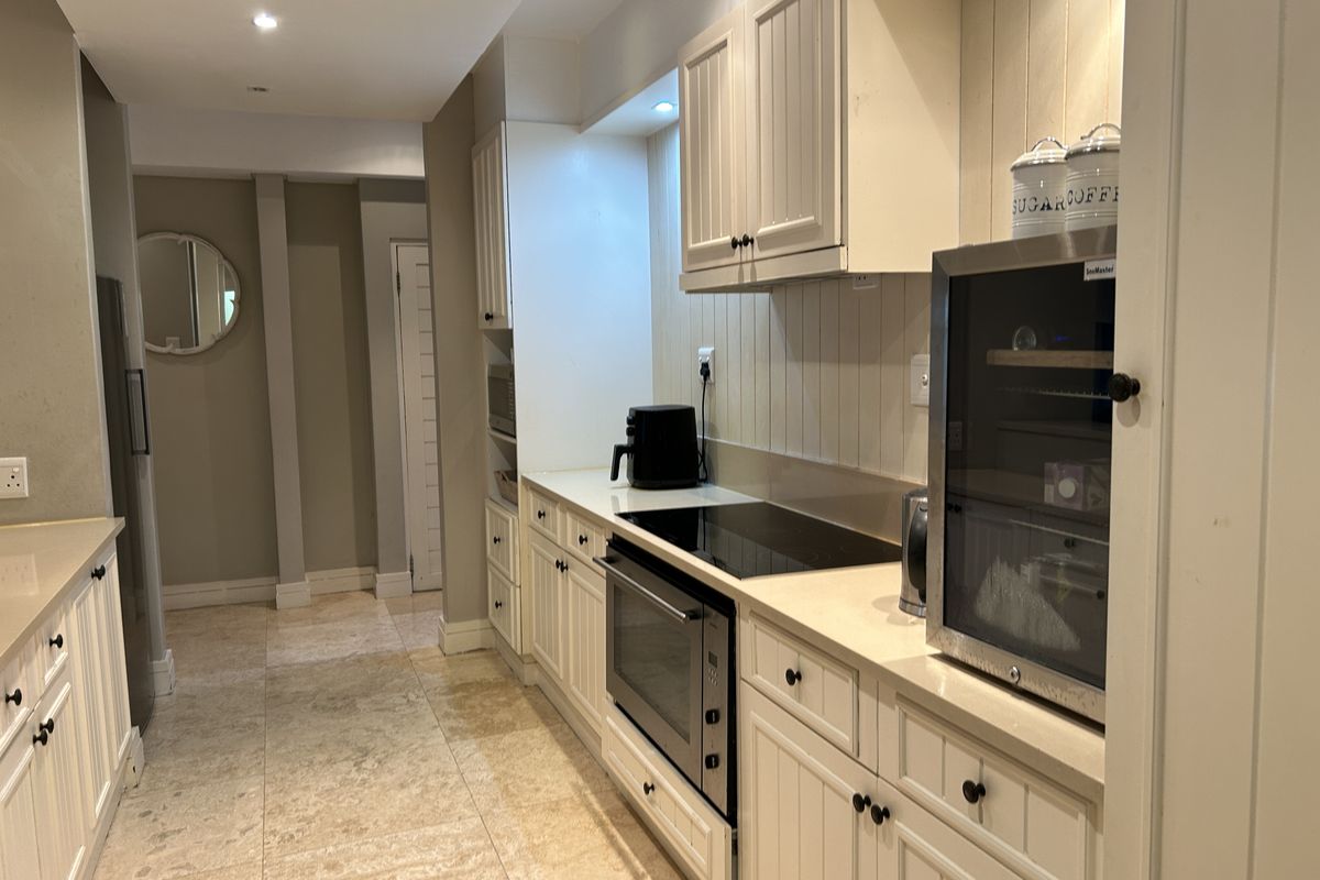A well-maintained kitchen featuring classic white cabinetry, stone countertops, integrated appliances, and stone floor tiles with recessed lighting.