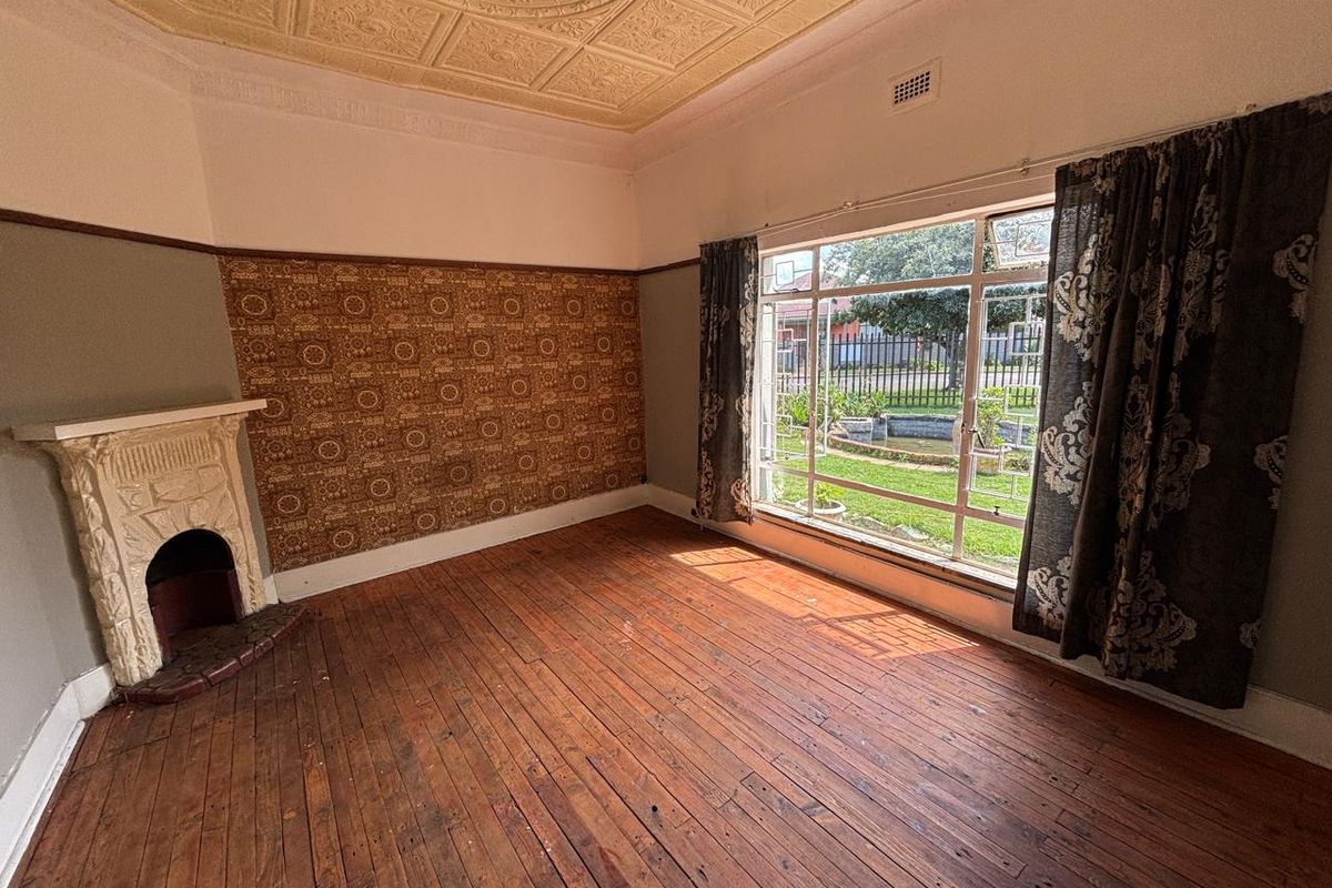 A spacious living room featuring original timber flooring, a decorative pressed metal ceiling, and a classic fireplace, offering a character-filled space with garden views.