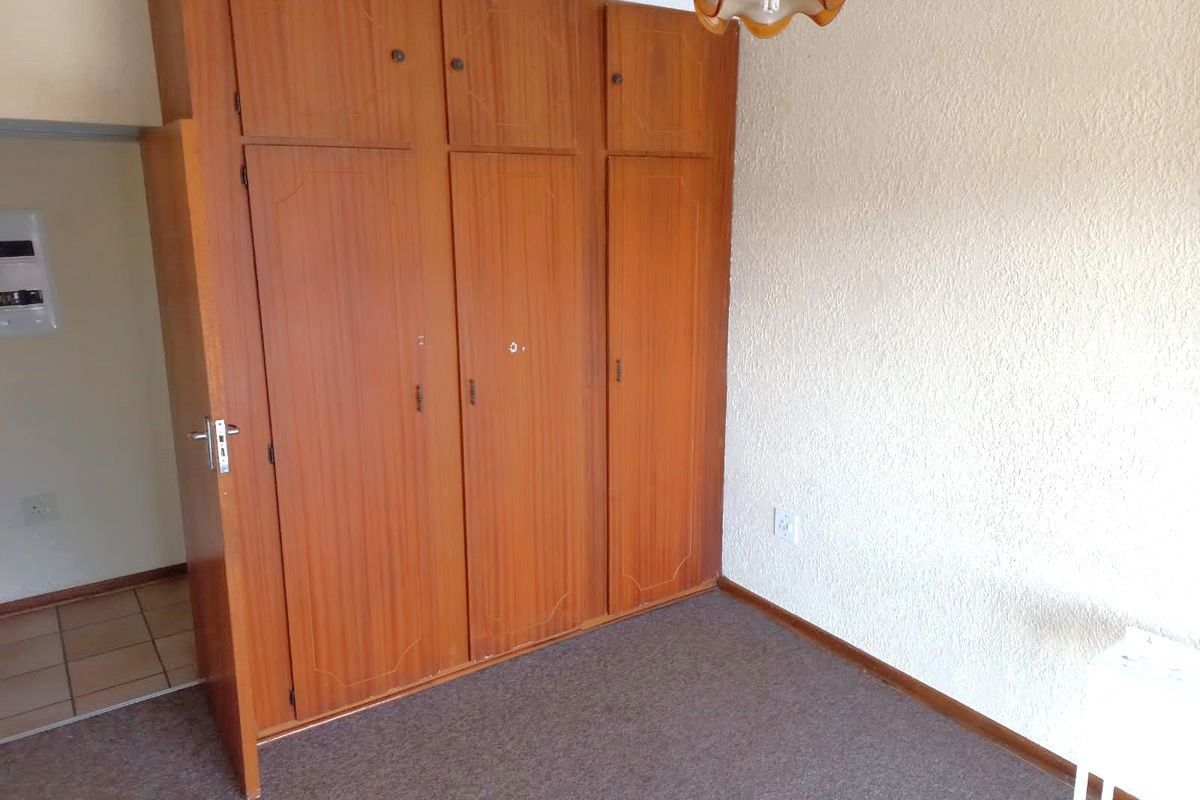 A bedroom featuring built-in wooden cupboards, textured walls, and carpeted flooring.