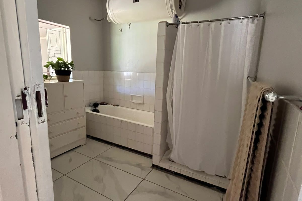 A functional bathroom featuring a built-in bathtub, separate shower enclosure, and wall-mounted geyser, finished with tiled flooring and wall splashbacks.