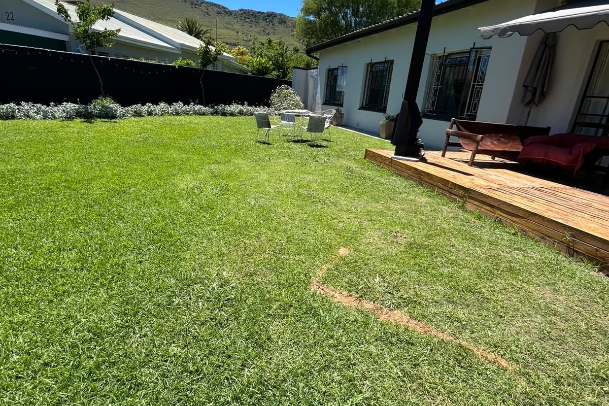 Spacious rear garden featuring a wooden deck, retractable awning, and outdoor fireplace, set against a scenic mountain backdrop.