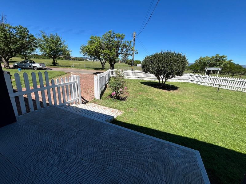 A well-maintained front garden featuring a white picket fence, brick paved driveway, and a tiled patio area overlooking a neat lawn.