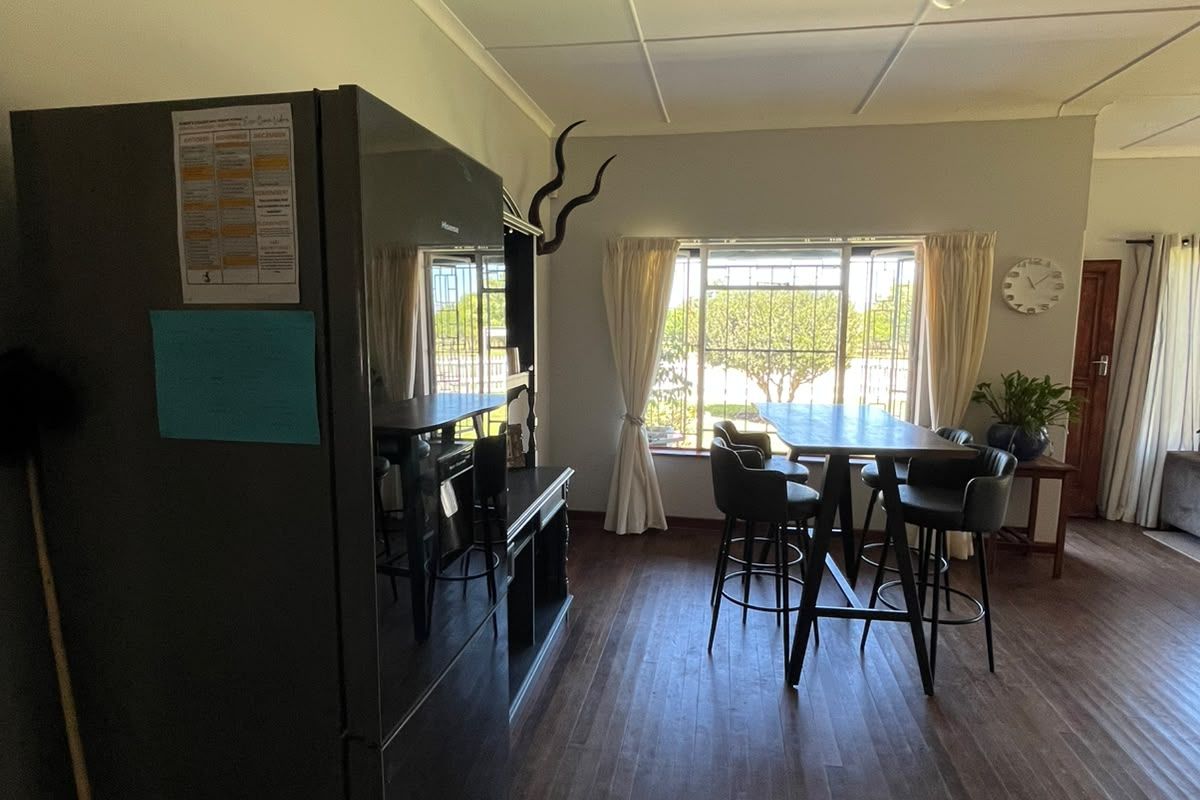 A living area featuring timber flooring, large windows with security bars, and a tiled ceiling, offering a functional space with natural light.