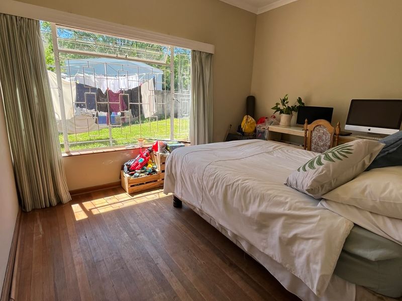 A bedroom featuring original hardwood flooring and a large window with security bars, offering natural light and a view of the rear garden.