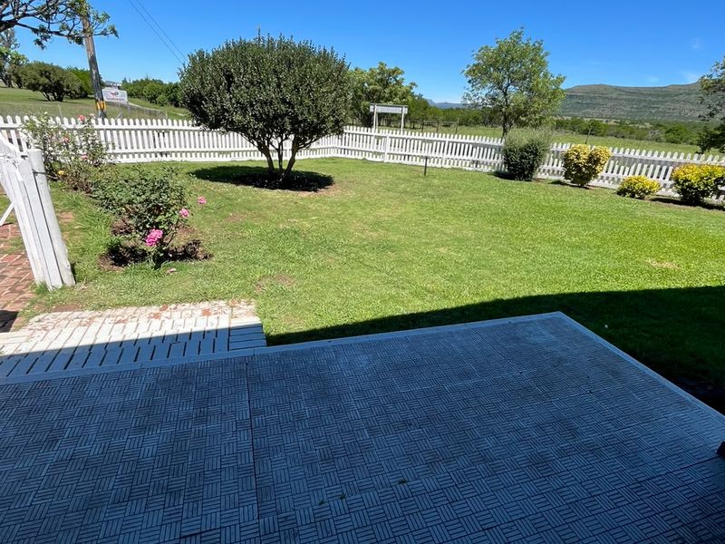 A well-maintained outdoor patio area featuring paved flooring, a white picket fence, and a neat garden with scenic mountain views.