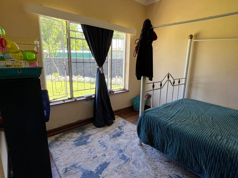 A bedroom featuring timber flooring, security bars on the window, and visible ceiling water damage requiring maintenance.