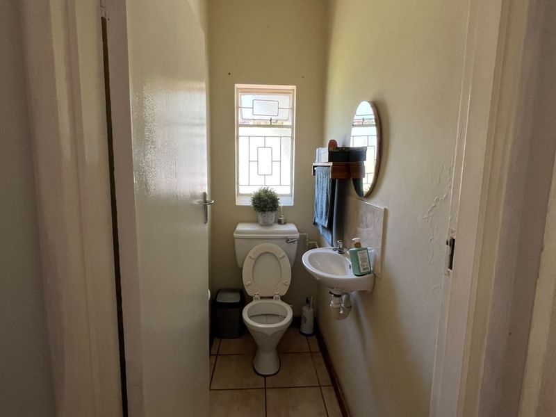 A compact guest bathroom featuring a wall-mounted basin, toilet, and tiled flooring, requiring minor cosmetic updates to improve its overall appeal.