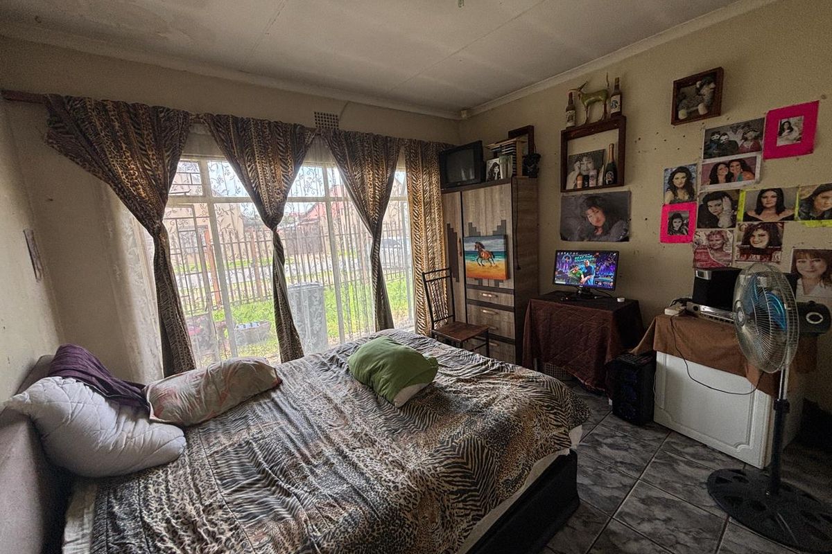 A bedroom featuring tiled flooring and a large window with security bars, requiring cosmetic updates to the walls and ceiling.