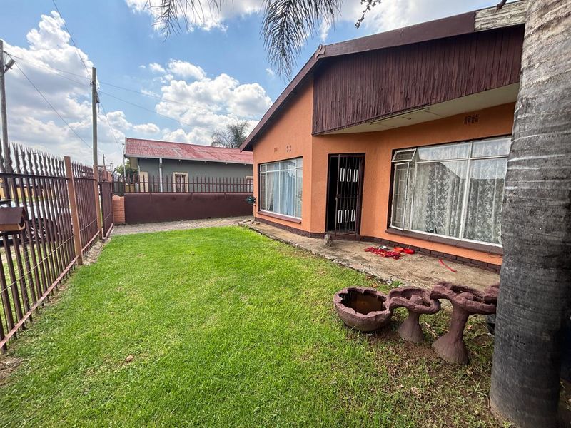 Front exterior view of the house featuring a lawn, paved walkway, metal security fencing, and aluminum window frames.