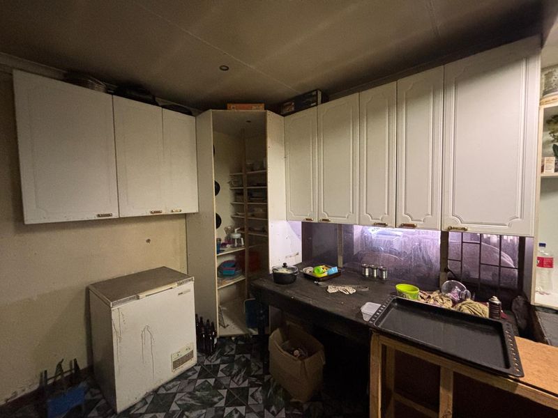 A dated scullery area featuring built-in cabinetry and a work surface, requiring cosmetic updates and repairs to improve functionality and aesthetic appeal.