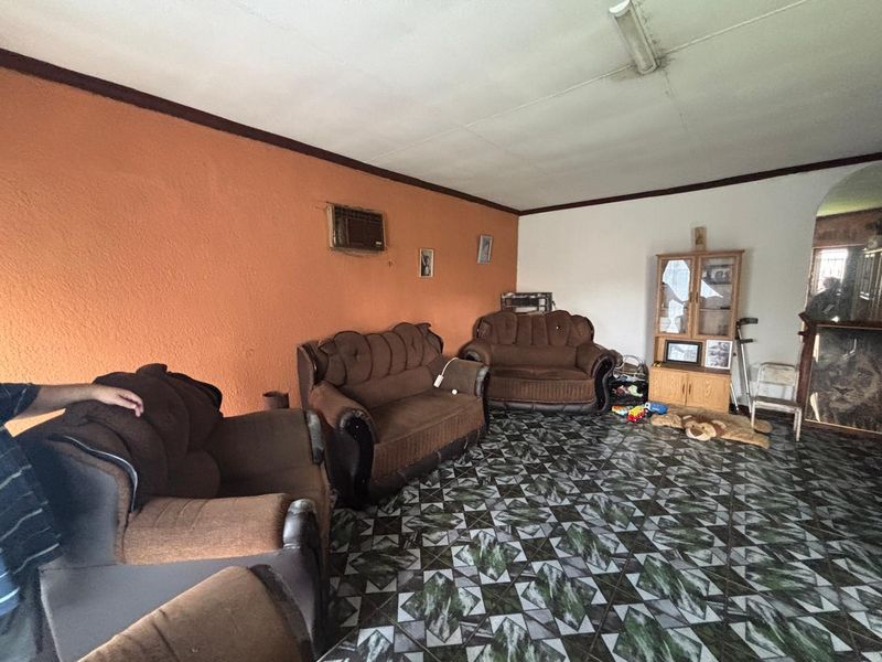 A living room featuring patterned tiled flooring and an integrated wall-mounted air conditioning unit, requiring cosmetic updates to improve the overall aesthetic.
